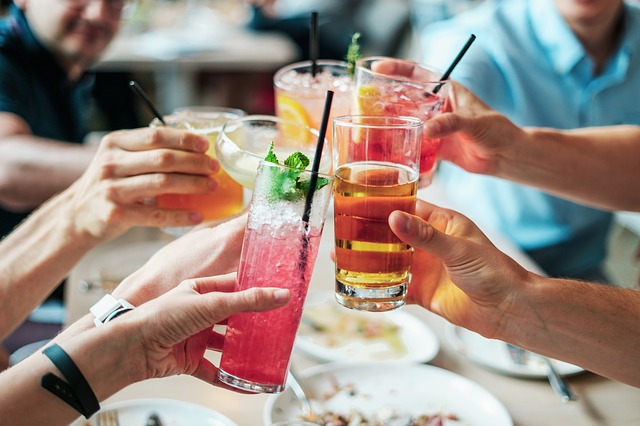 Auf dem Bild sieht man Hände, die bunte Cocktails und Getränke halten und miteinander anstoßen