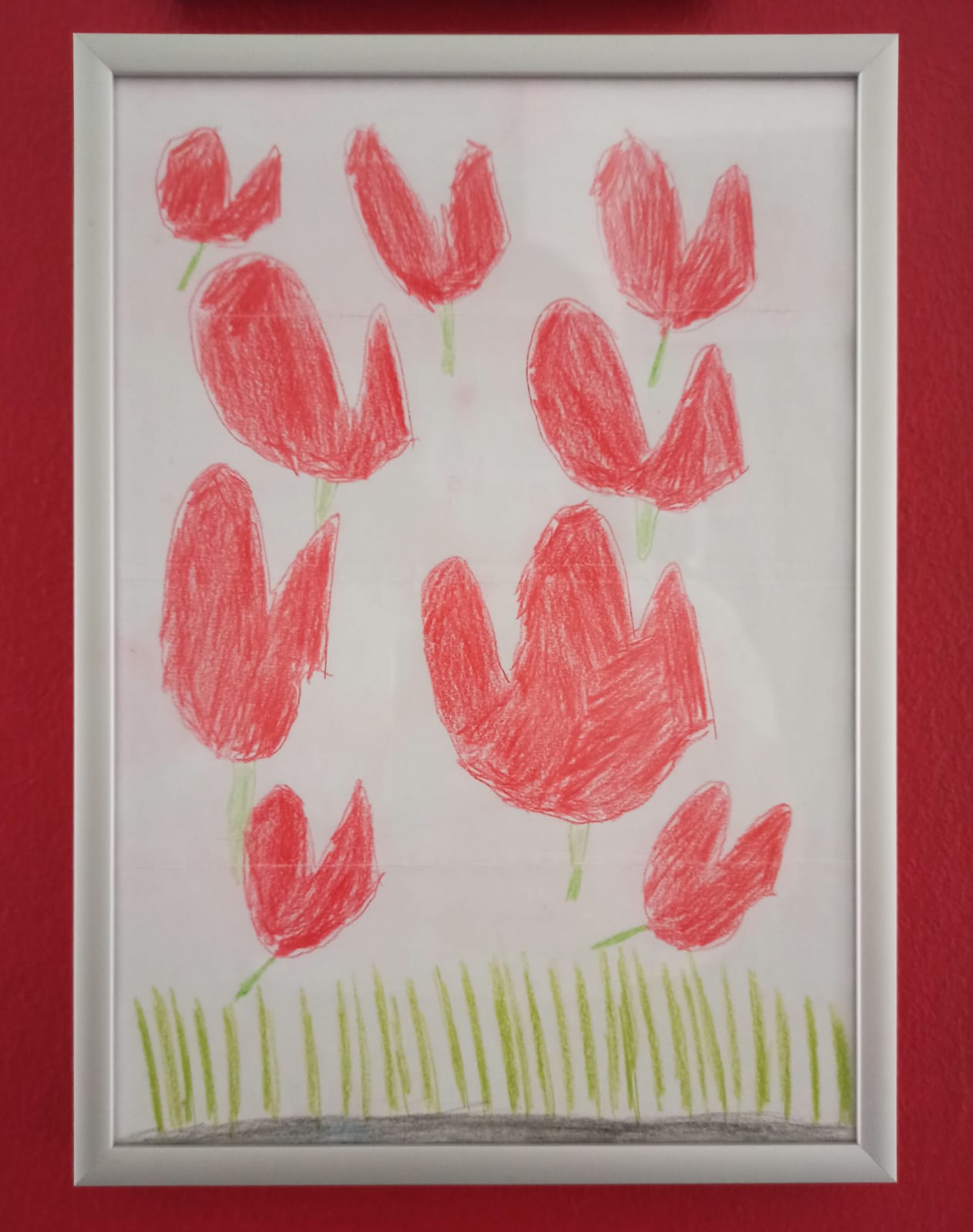 Ein Bilderrahmen auf roter Wand. Das Bild zeigt Wiese und rote Tulpen und Herzen.